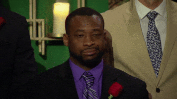 Reality TV gif. A man from The Bachelorette is standing with all the other men and he does a side eye towards the other contestants while showing a disappointed smirk on his face. 