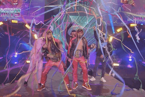 Gif of two long-haired white men dressed in leather wearing boxing belts being showred by confetti strings, squaring up to the camera and saying "you're looking at the best"