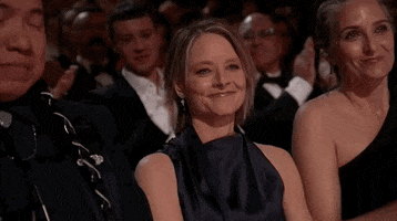 Oscars 2024 GIF. Jodie Foster, seated at the Oscars, uses both hands to blow a kiss of self-confident friendly gratitude.