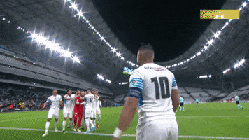 Sports gif. Dimitri Payet walks towards his teammates, who high-five and hug him.