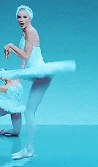 Music video gif. Taylor Swift in the video for Shake It Off. She's dressed as a ballerina and is doing a backwards bunny hop across the stage.