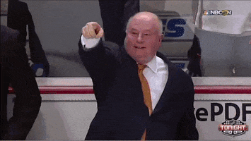 Sports gif. On the sidelines of a hockey game, an older man in a suit points offscreen repeatedly, growing more enthusiastic as he does.