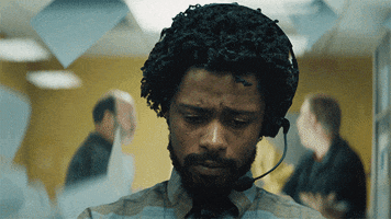 Movie gif. Looking sad, LaKeith Lee Stanfield as Cassius in Sorry to Bother You concentrates on his work, wearing a headset. Chaos reigns in the background as papers fly up and people argue.