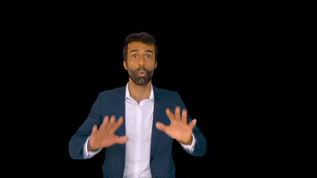 Homem de terno azul em um fundo preto gesticulando com as mãos para frente, como se estivesse enfatizando um ponto ou pedindo calma.