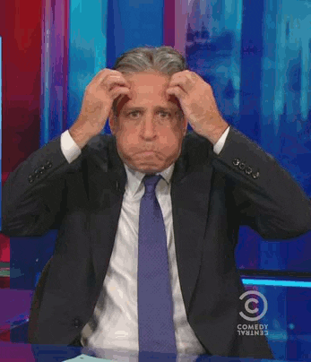 TV gif. Jon Stewart on The Daily Show blows his cheeks up with air and holds both hands to the side of his head, moving them in an exploding motion as he opens his mouth as if to say, “Mind blown.”