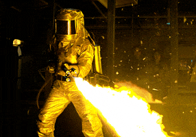 Video gif. A person in a silver fire-resistant safety suit shoots flames from a backpack flamethrower.