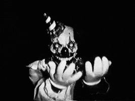 Video gif. Black and white footage of a scary clown with a toothy grin as he reaches his hands out and beckons for us to come closer.