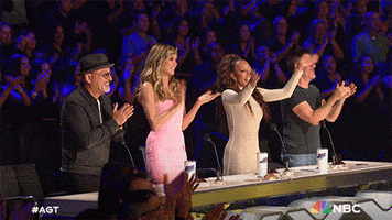 Reality TV gif. The judges on America's Got Talent are all on their feet and applaud enthusiastically as they give the contestant a standing ovation.