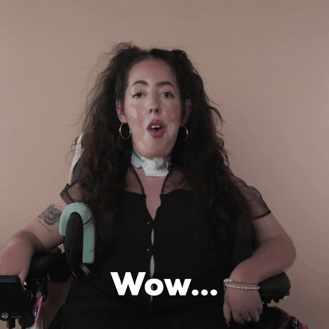 Reaction gif. A Disabled white woman with muscular dystrophy with wavy brown half up half down with two pigtails on top, seated in her motorized wheelchair, rolls her eyes and coolly says "Wow."