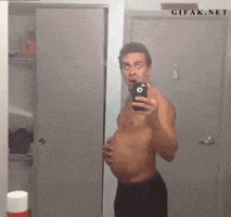 Video gif. A man standing in front of a mirror pushes his belly out, making it round, his eyes bulging. He then turns and smiles, tensing his abs and showing off his defined muscles.