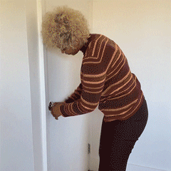 Video gif. A woman is trying to leave a room but the door handle is stuck. She finally jimmies it open and the force of it pushes her back. She leaves the room but turns around to give us a smile and a thumbs up. Text, "Coming out is hard. But it's worth it!"