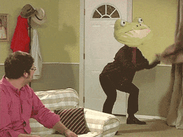 Video gif. A man with a superimposed frog head squats and swings a jacket back and forth between his legs as another man looks on.