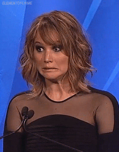 Celebrity gif. Jennifer Lawrence grimaces in front of a microphone during a panel as if to say, "Yikes!"