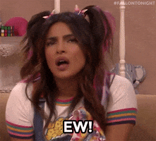 Celebrity gif. Priyanka Chopra is playing a teenager in a skit and has multi colored hair in pigtails and glitter eyeshadow. She gives us a disgusted look before jutting her head out and saying, "Ew!"