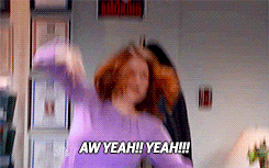 The Office gif. Ellie Kemper as Erin stands behind the reception desk and pumps her fist in a fit of excitement as she yells, “Aw yeah! Yeah!” Angela Kinsey as Angela Martin looks on at her from her desk.
