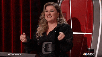Celebrity gif. Kelly Clarkson on The Voice is absolutely ecstatic as she stands up from her red chair, pumps her fists, and screams in excitement.
