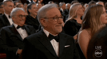 Oscars 2024 GIF. Steven Spielberg, seated at the Oscars, shifts his gaze from the stage, into space, then to us, staring vacantly in dumbfounded disbelief.