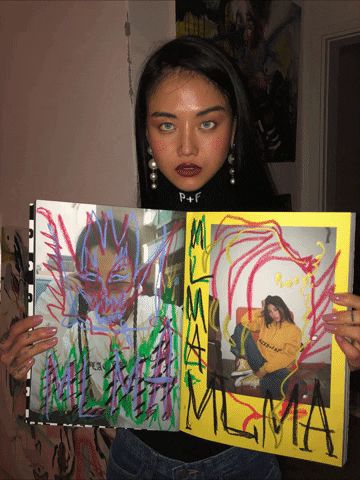 Celebrity gif. MLMA, a South Korean artist, is holding up an art book of herself. Her eyes have been edited to roll around in all directions as everything else stays completely still.