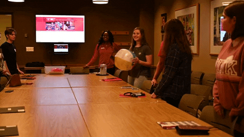 Students pass a beach ball to each other around a boardroom table.