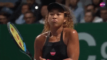 Sports gif. Naomi Osaka is on the tennis court holding her racket and she frowns deeply while lifting her arms into a shrug.