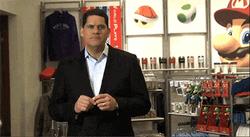 Video game gif. Man in a suit talks to us inside a Super Mario merchandise store when Luigi accidentally walks in from the side and slaps his hand over his mouth in embarrassment before making a quick exit.