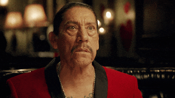 Ad gif. Actor Danny Trejo in a Magic the Gathering commercial sits at a restaurant table in a red velvet smoking jacket. He kisses his finger tips in a gesture expressing perfection. 