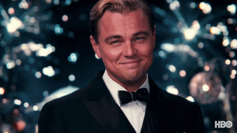 Leonardo DiCaprio v gifu zvedající číši se šampaňským k přípitku na pozadí vybuchujících ohňostrojů. 