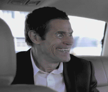 Celebrity gif. Willem DaFoe sitting in a car, with confused eyes and a huge, unnerving grin.