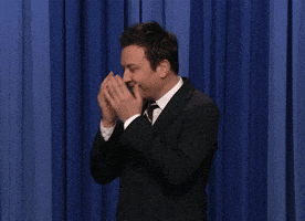 TV gif. Jimmy Fallon stands in front of a blue curtain, burying his face in his hands, then lowering his hands and shaking his head, looking down, embarrassed.
