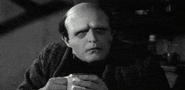Movie gif. In black and white, Mel Brooks as Victor in Young Frankenstein stoically holds out a mug to cheers with as a large hand holding another mug slams into Victor’s mug, shattering it as liquid explodes, leaving Victor holding only the mug handle as he sighs and rolls his eyes in annoyance.