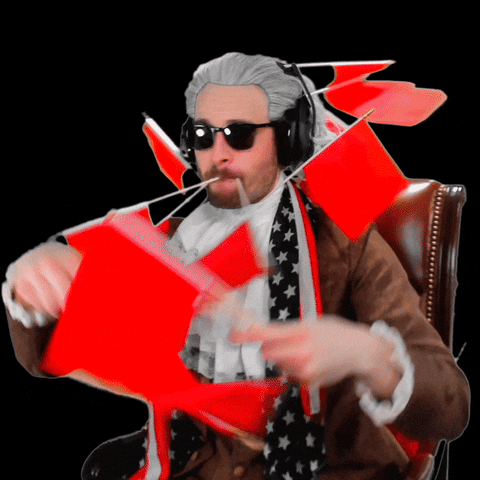 Video gif. Man wearing a gray wig, sunglasses, and headphones is dressed in historical colonial clothing with an American flag wrapped around his neck. He's swathed in a bunch of red flags, some coming out of his mouth. He waves some wildly before tossing them to the side. 