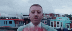 Celebrity gif. Macklemore is wearing a teal suit and he puts a red helmet on his head before disappearing. 