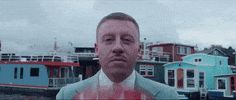 Celebrity gif. Macklemore is wearing a teal suit and he puts a red helmet on his head before disappearing. 