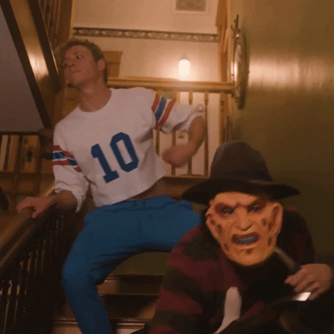 Music video gif. Dressed like a slutty football player, IAmNotShane dances while descending a staircase following behind Freddie Krueger, who waves his claws menacingly at us.