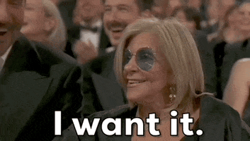 Oscars 2024 GIF. Gloria Campano raises her hand, wagging her finger in the air, calling, “I’ll take it!”