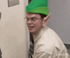 The Office gif. Rainn Wilson as Dwight wears a green elf hat and pointy ears as he looks at someone off screen and gives a thumbs up, his tongue sticking out slightly.