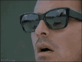 Video gif. An extreme close-up of a man's face shows him slowly removing his black sunglasses in awe.