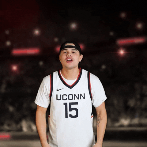 Video gif. Man in a UConn basketball jersey and a backwards black hat stands on a basketball court as he yells and claps to us. Text, "C'mon UConn. Bring that Natty Home."