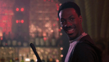 Movie gif. Eddie Murphy as Axel Foley in Beverly Hills Cop 4 makes an "OK" sign with his hand, the camera zooming in and freeze framing, before zooming out in front of shelf of wine bottles.
