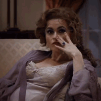 Movie gif. Helena Bonham Carter as Elizabeth Taylor in Burton and Taylor, reclines against a chair while wearing loungewear, blowing us a kiss seductively and winking.