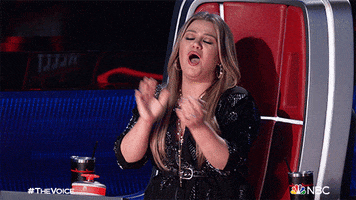 TV gif. Kelly Clarkson on The Voice. She's sitting in her judges chair and she claps enthusiastically while whooping.