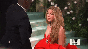 Met Gala 2024 gif. Shakira wearing a red Carolina Herrera gown in slomo, looks down briefly, in stoic sadness.