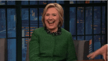 Political gif. Hillary Clinton leans forward as her mouth gapes open in laughter before she settles back in her chair.