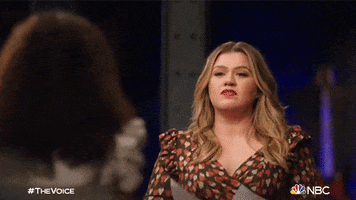 Reality TV gif. Kelly Clarkson on The Voice smirks as she dances as if she is really into the song. 