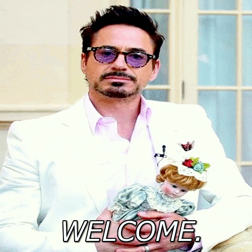 Celebrity gif. Robert Downey, Jr. wears a white suit and holds a porcelain doll as his tilts his head and says, "Welcome."