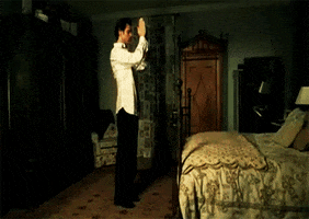 Movie gif. Jim Carrey as Bruce in Bruce Almighty stands fully dressed at the foot of a bed with his hands clasped together, then whips his arms down by his sides as his clothes swiftly drop to the floor.