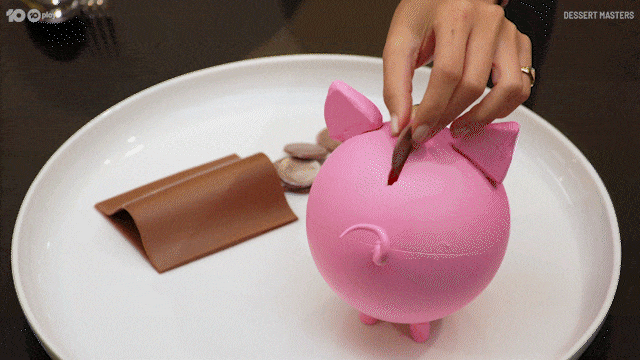 A hand dropping a coin into a pink piggy bank