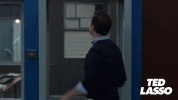 TV gif. Jason Sudeikis as Ted in Ted Lasso, reaches up to a sign over the door frame and slaps it as he exits. The sign says, "Believe" in sharpie. 