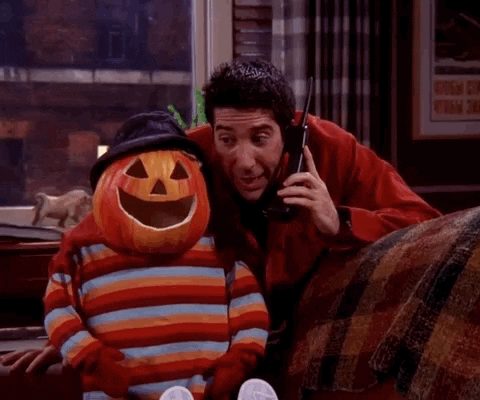 Friends gif. David Schwimmer as Ross talks on a phone, then holds it up to the ear of a jack-o-lantern headed figure sitting beside him.