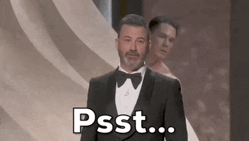 Oscars 2024 GIF. A potentially nude John Cena is behind a wall on stage and he tries to get Jimmy Kimmel's attention by saying, "Pssst!" Kimmel looks left and right, trying to find where the noise is coming from.
